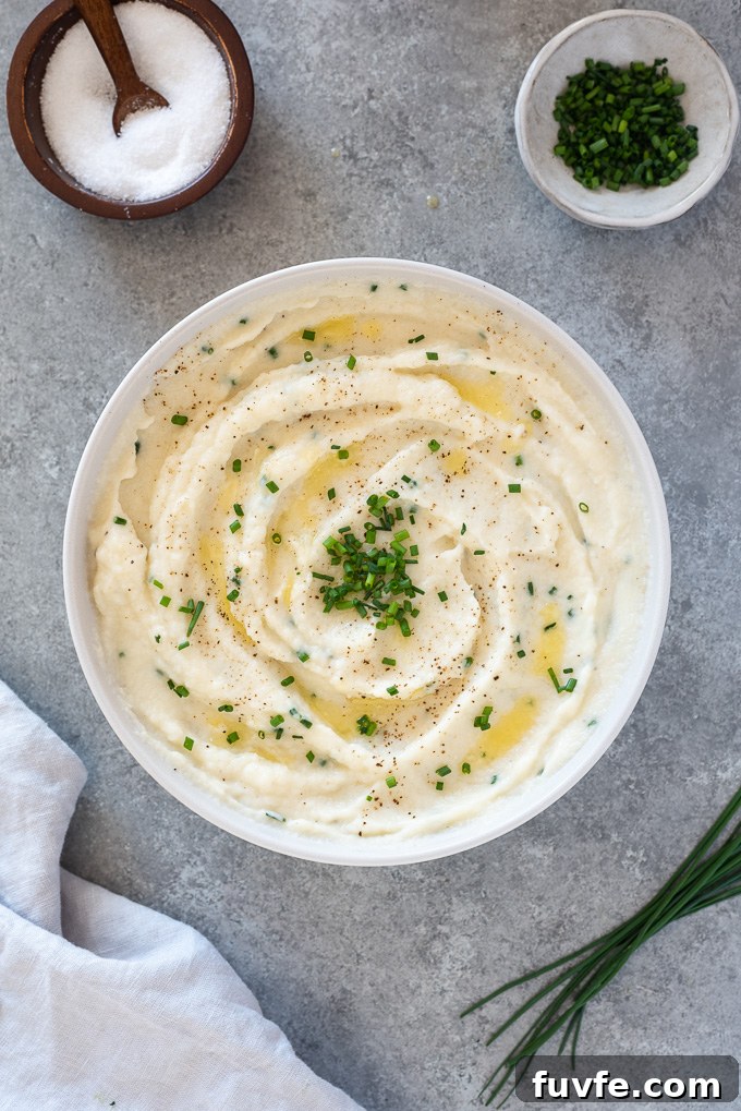 Garlic mashed cauliflower in a white serving bowl with chives