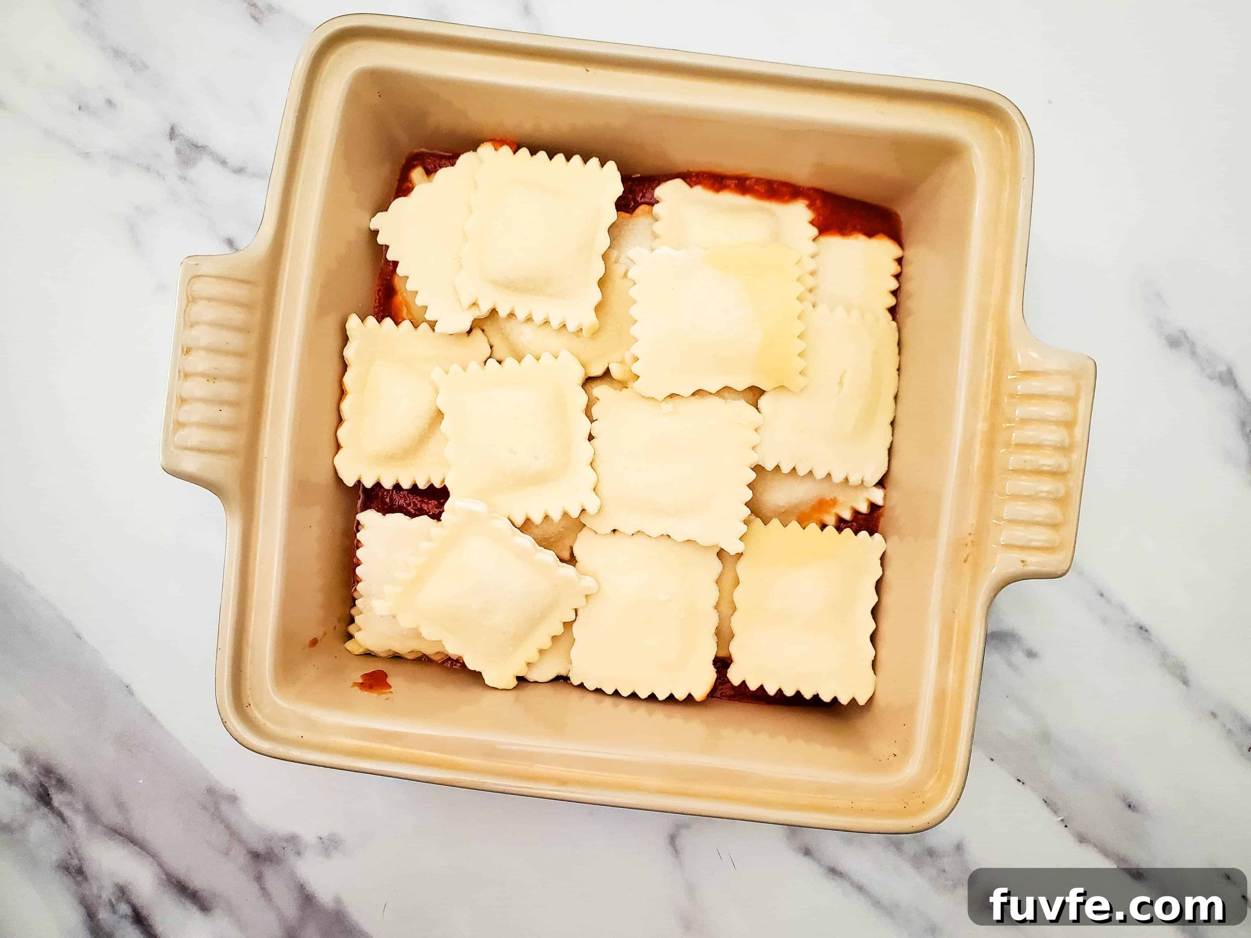 Quick Ravioli Lasagna Recipe for Fast Weeknight Dinners 5 Glass baking dish with pasta sauce and frozen ravioli on top of a white counter