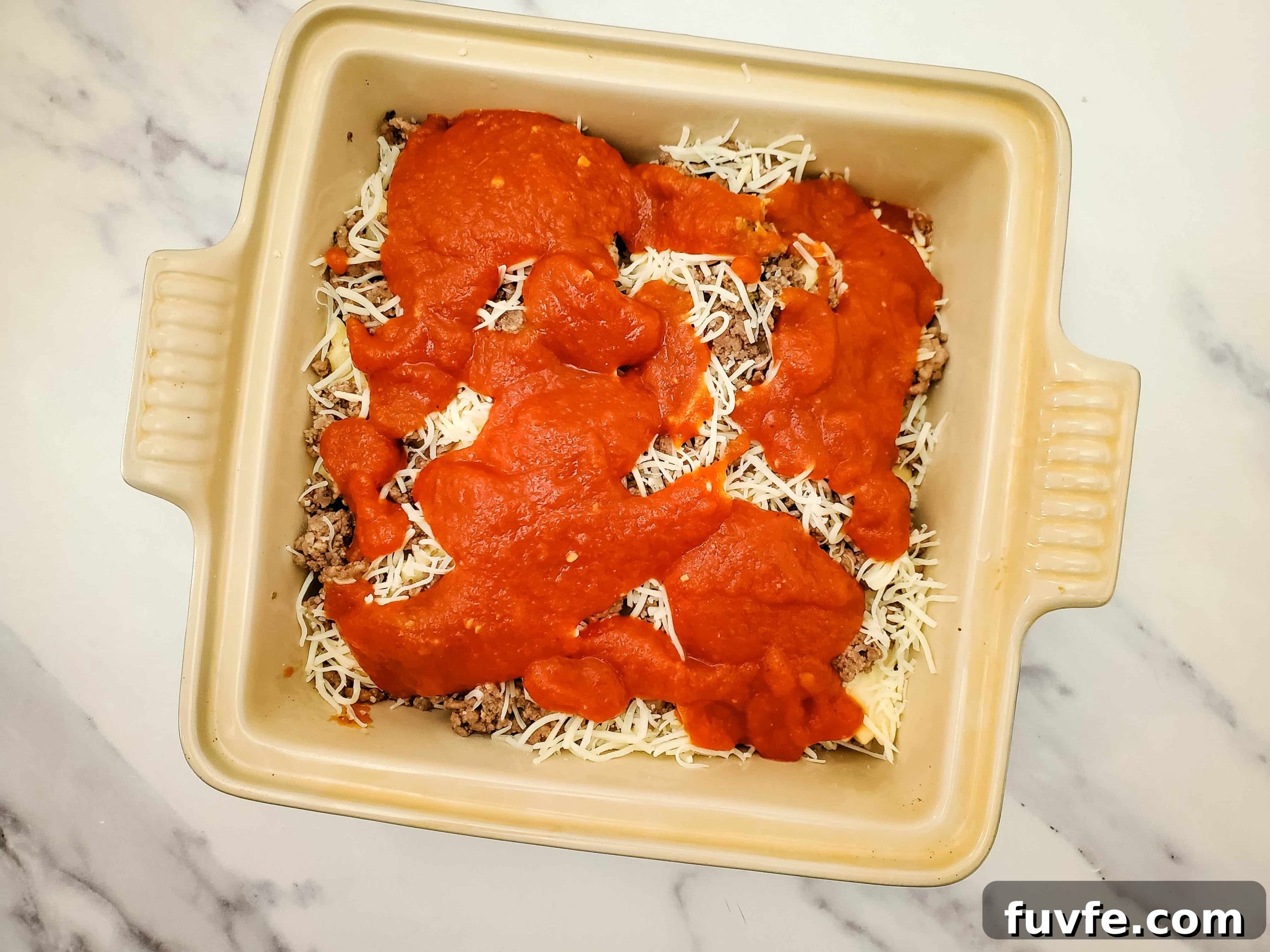 Quick Ravioli Lasagna Recipe for Fast Weeknight Dinners 7 Casserole baking dish with layered frozen ravioli recipe and pasta sauce on top of a marble counter
