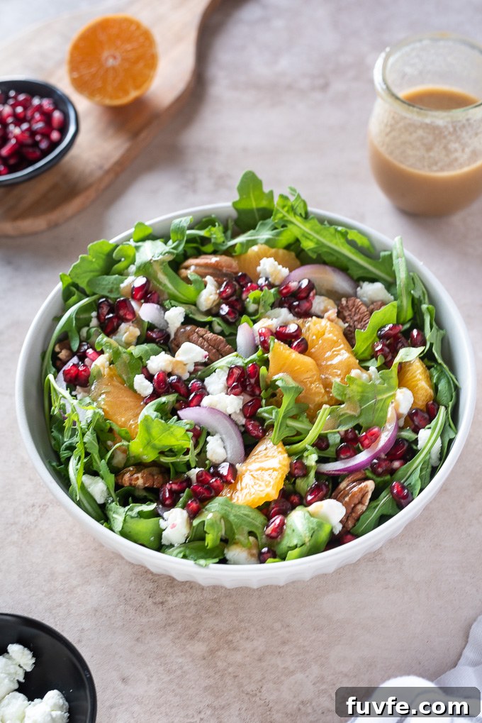 Arugula orange pomegranate salad in a white bowl with pecans on top