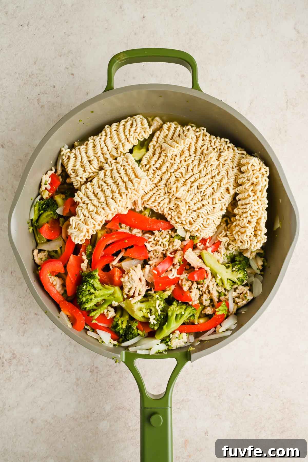 cooked veggies and ground chicken in skillet with raw ramen noodle blocks.