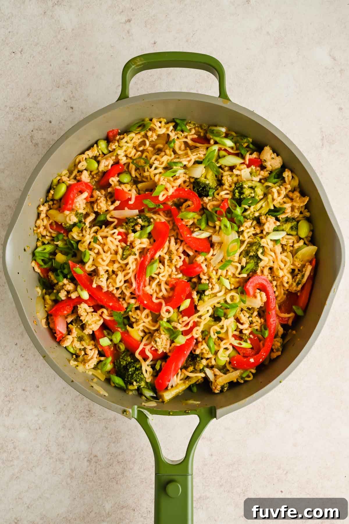 upgraded ramen with peppers, broccoli and edamame in green skillet.