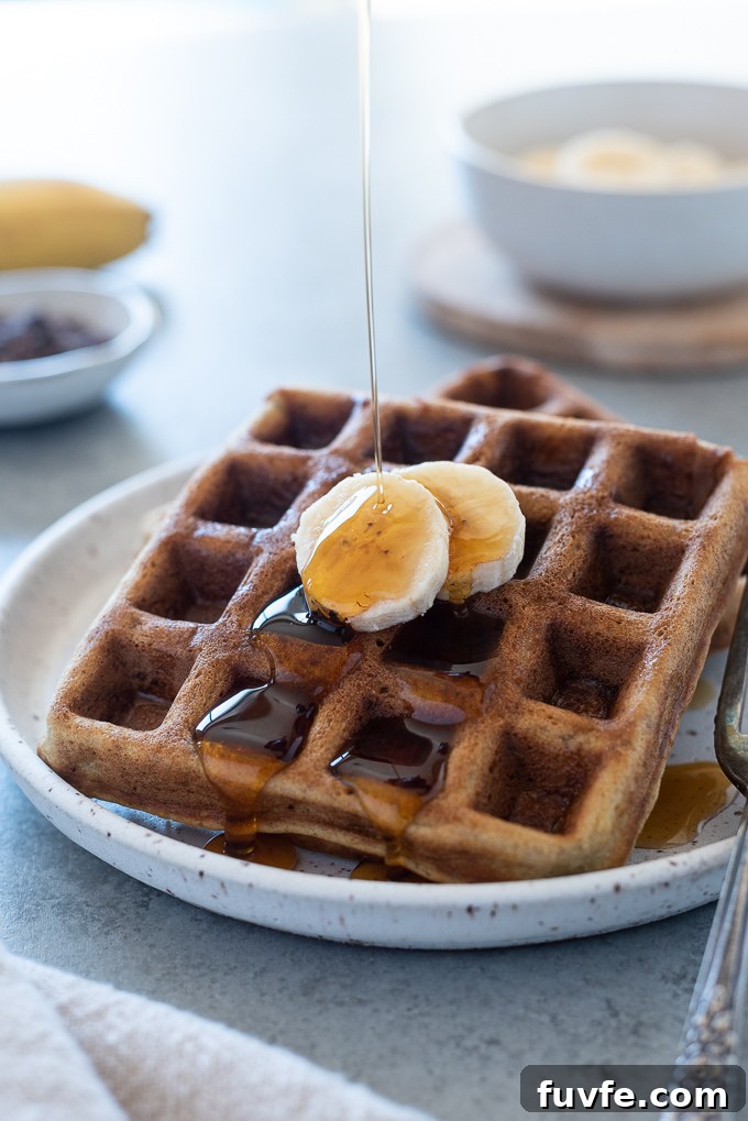 Syrup pouring over a small stack of banana waffles