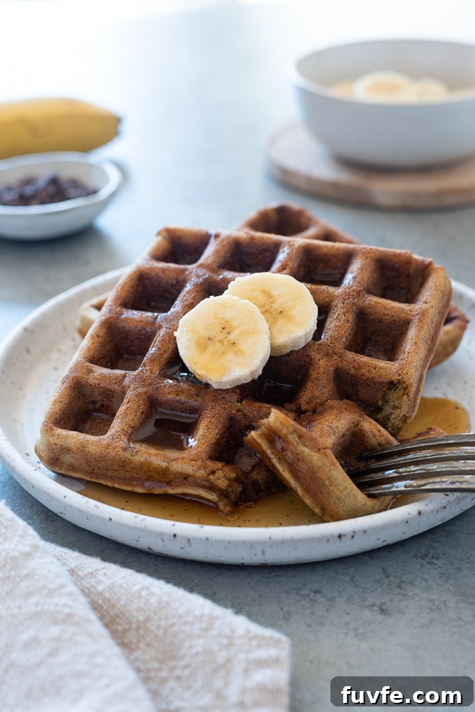 Banana oatmeal waffles on a plate with sliced banana and maple syrup