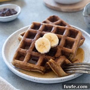 Banana waffles on a plate with sliced banana on top