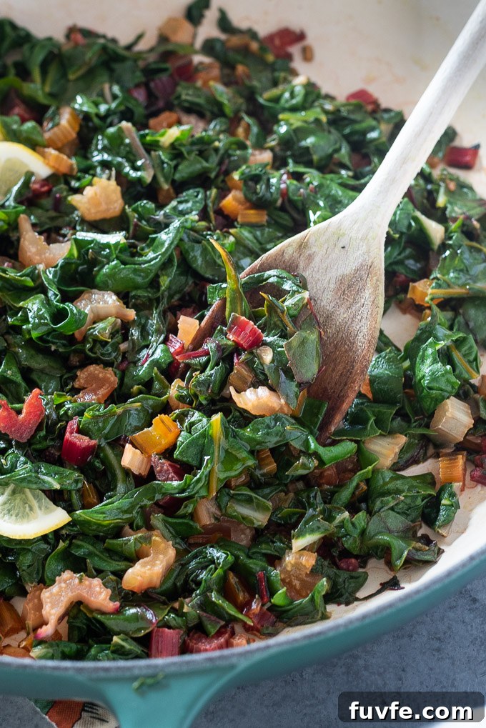 Wooden spoon digging into a Dutch oven filled with sautéed Swiss chard
