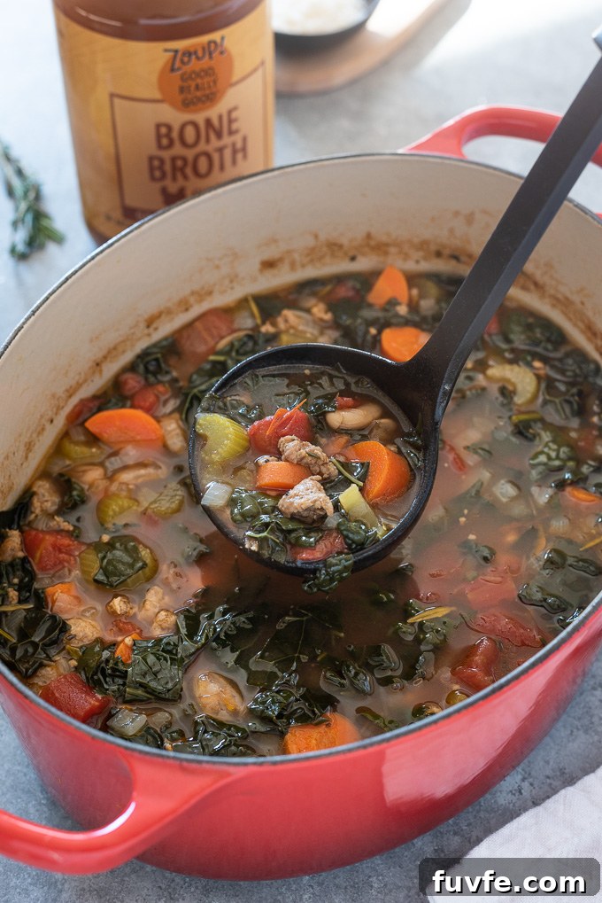 Ladle full of sausage and kale soup over a Dutch oven