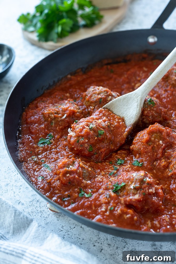 Wooden spoon digging into a skillet of oven baked meatballs and sauce