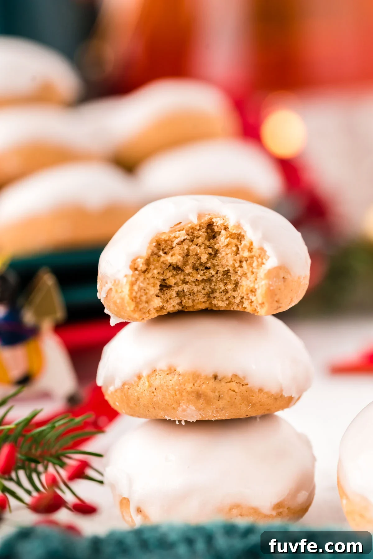 Close up photo of three pfeffernusse cookies stacked on top of each other with holiday decorations in the background.