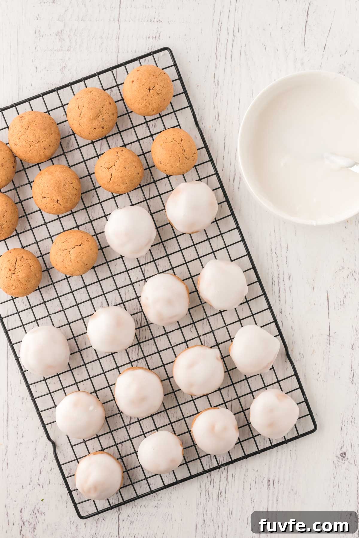 Cookies on a wire rack some iced, some not. Bowl of icing to the side.