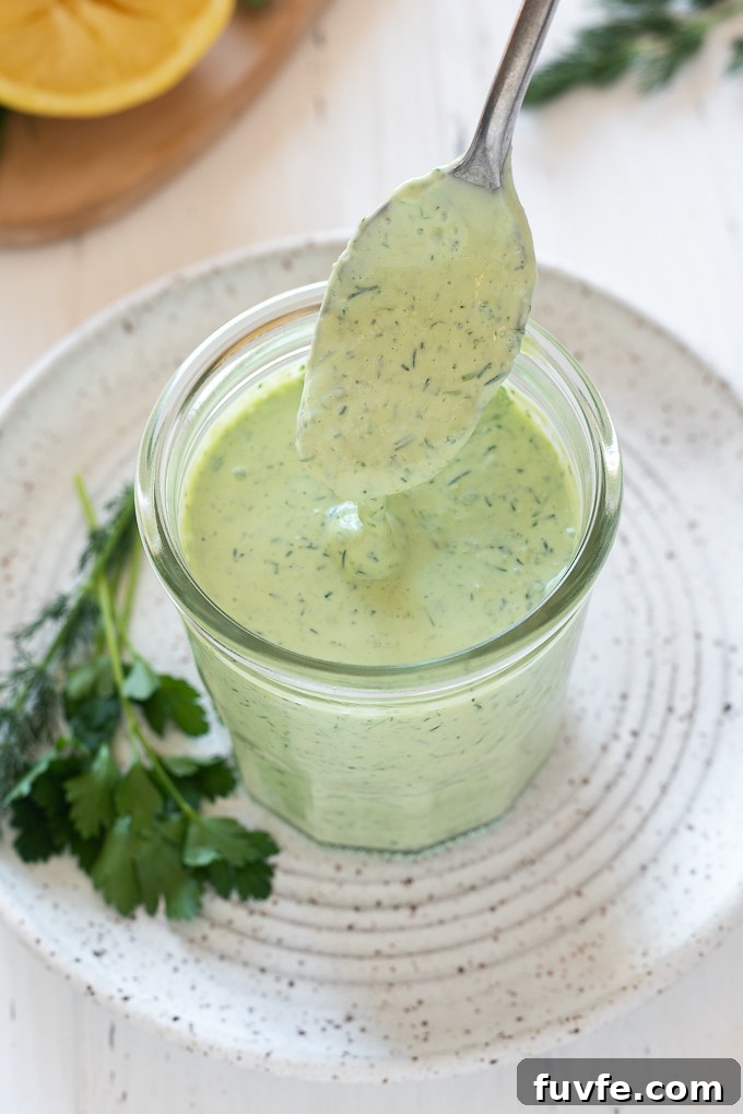 Green goddess dressing drizzling from a spoon into a jar