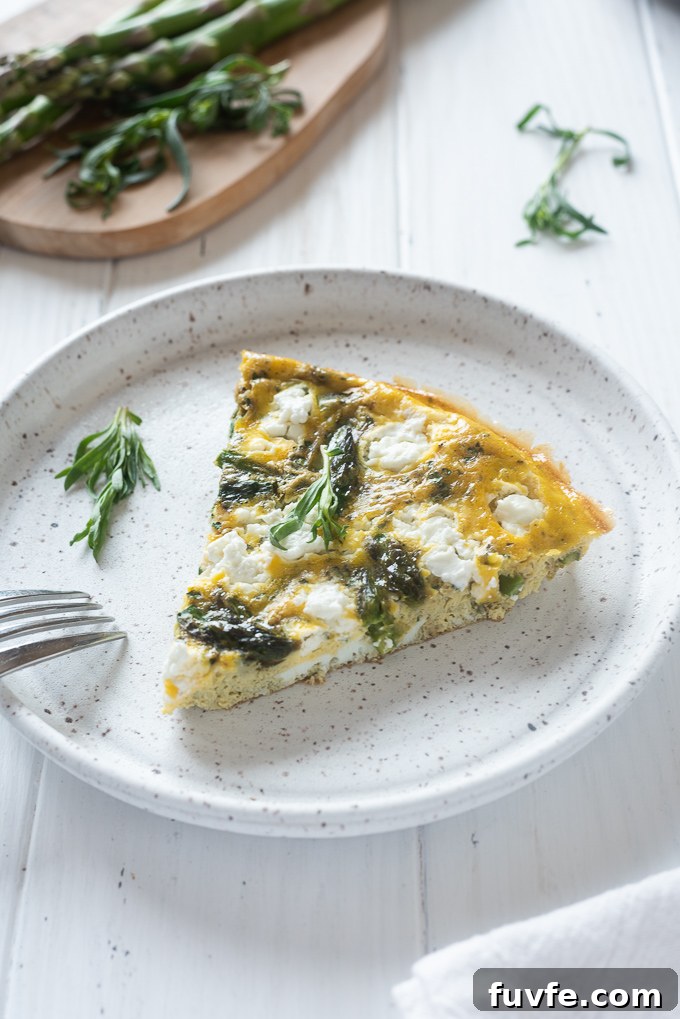 Slice of asparagus frittata on plate with tarragon sprig