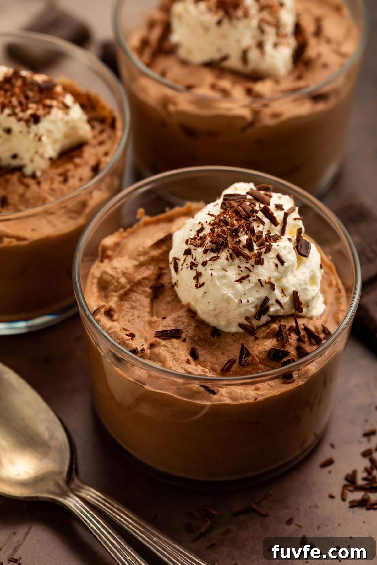 Low-Carb Keto Chocolate Mousse Recipe for Rich Guilt-Free Dessert 2 Three glass cups of keto chocolate mousse topped with keto whipped cream and chocolate shavings.