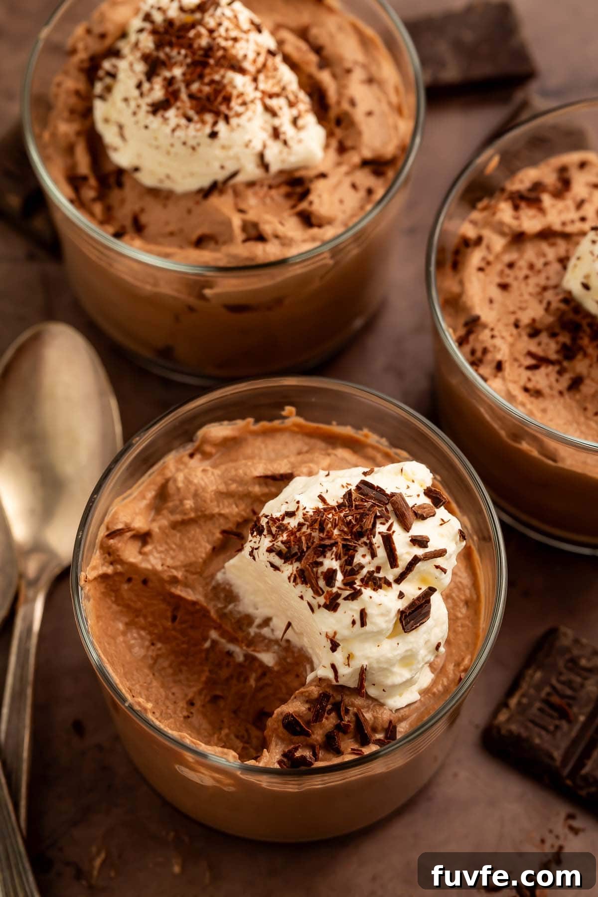 Low-Carb Keto Chocolate Mousse Recipe for Rich Guilt-Free Dessert 3 Three glass cups of keto chocolate mousse topped with keto whipped cream and chocolate shavings.