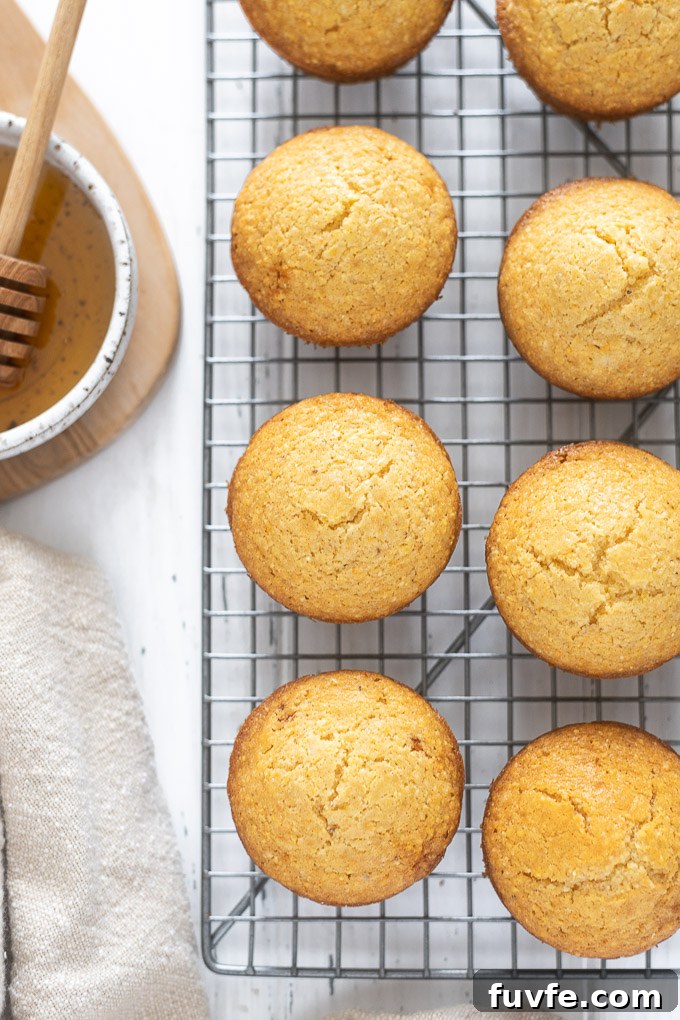 Fluffy Honey Cornbread Muffins Recipe 6 Corn muffins on a wire rack next to bowl of honey