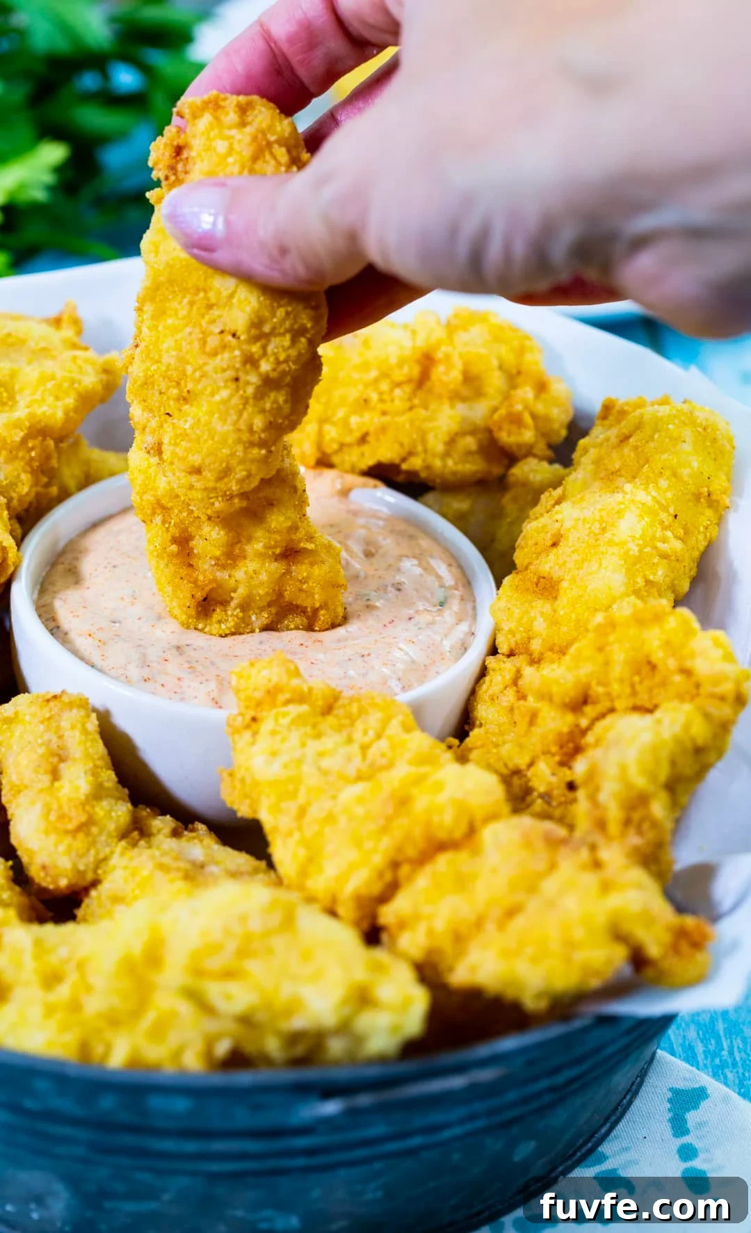 Hand dipping catfish finger into remoulade.