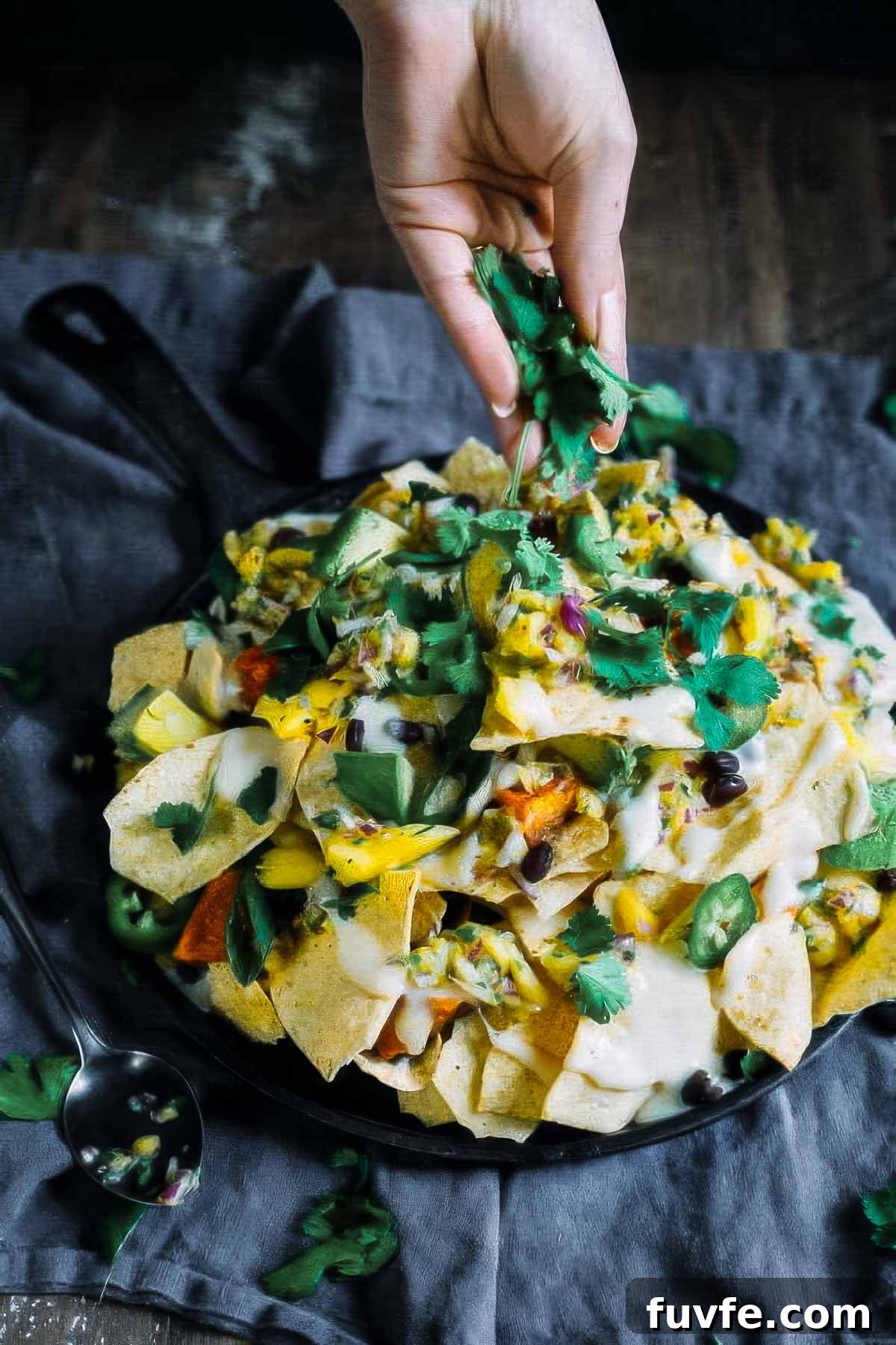 a plate of sweet potato nachos on a black linen towel with fresh cilantro being sprinkled on the top