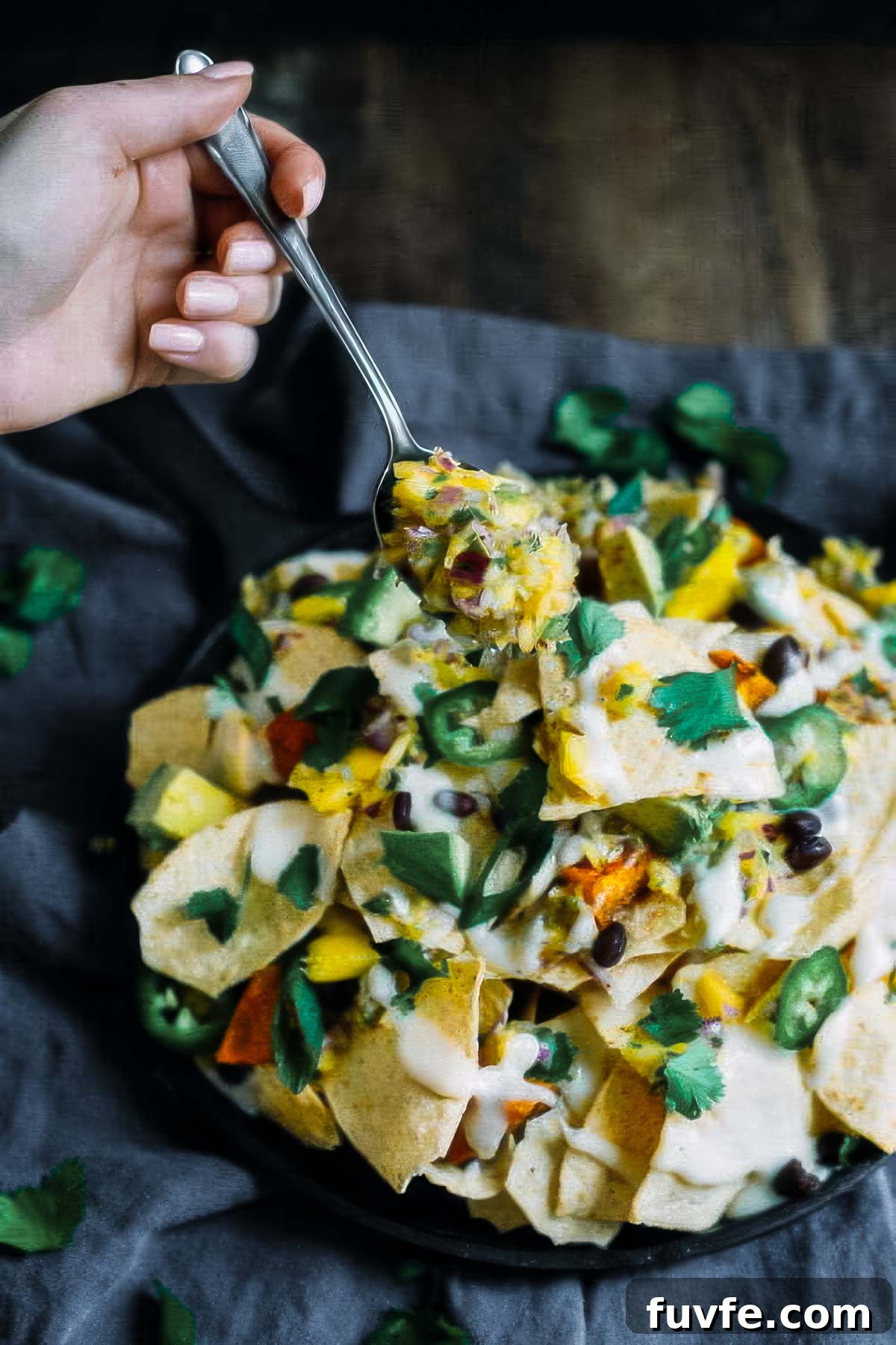 a plate of sweet potato nachos on a black linen towel with a serving being scooped out with a spoon