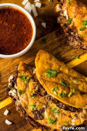 top down view of two birria tacos on a wooden board next to a small bowl of consommé