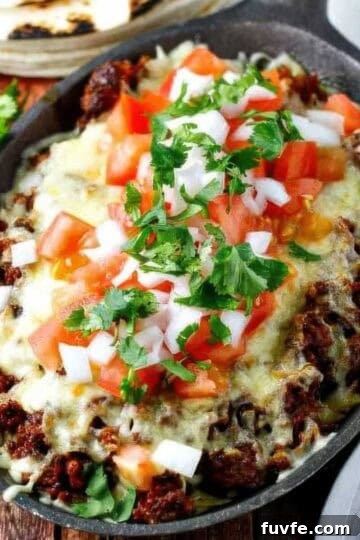 a cast iron skillet filled with choriqueso made with chorizo and cheese then topped with diced tomato, white onion, and cilantro