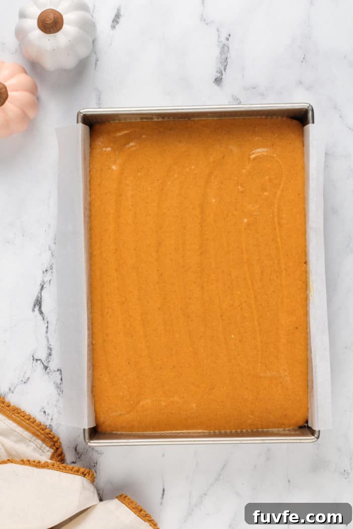Pumpkin Gooey Butter Cake Recipe — Decadent Fall Dessert 9 Assembled pumpkin gooey butter cake in a parchment-lined pan, ready to go in the oven.