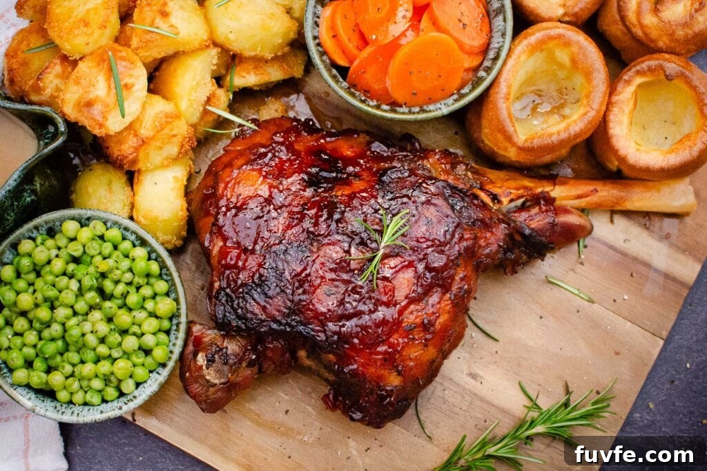 Slow Cooked Leg of Lamb on a wooden board with peas, roast potatoes, carrots and Yorkshire puddings