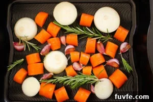 Chopped onion carrots garlic cloves and sprigs of thyme in a roasting tray