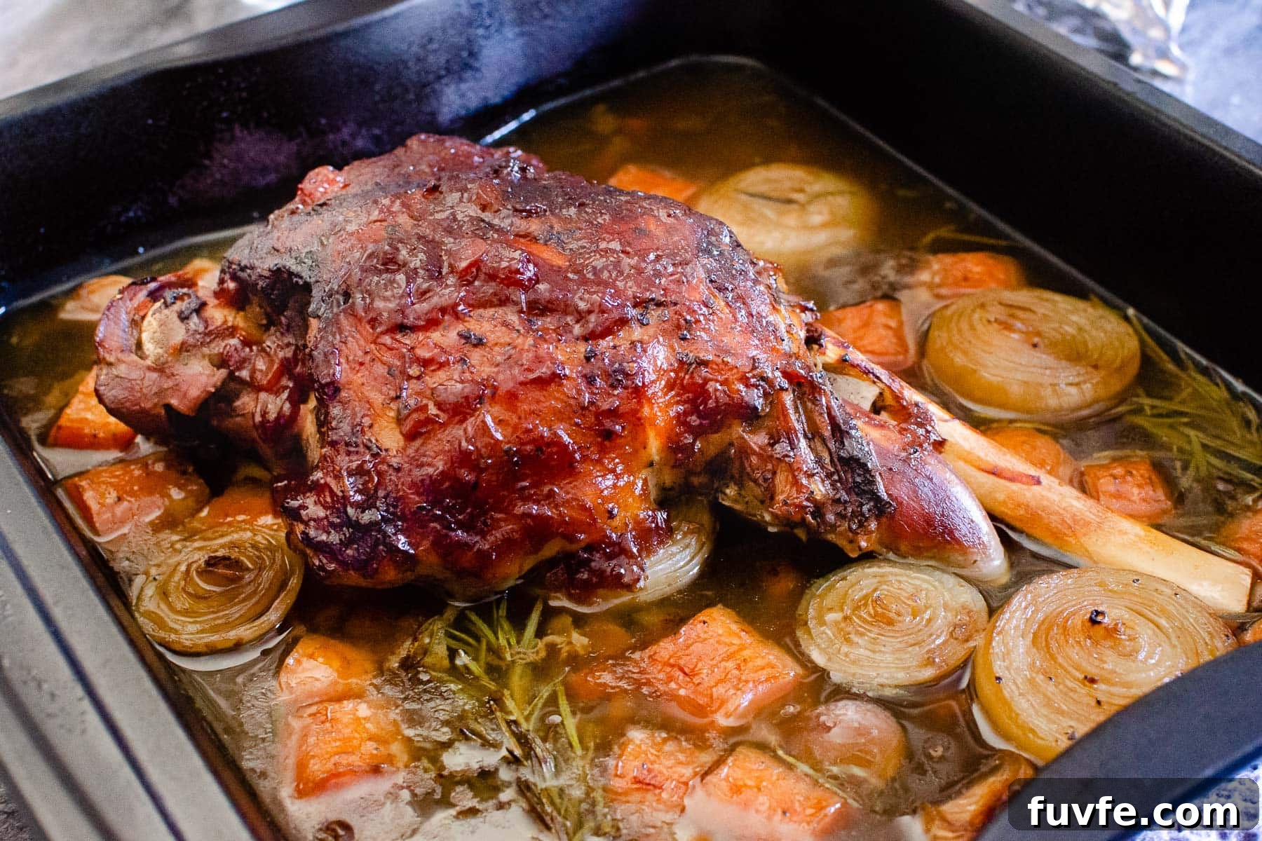 Cooked Slow Cooked Leg of Lamb in a roasting tray in stock and chopped veg