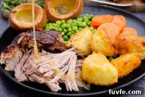 Slow roast leg of lamb served with roast potatoes, carrots,peas and Yorkshire puddings and lamb gravy being poured over the top