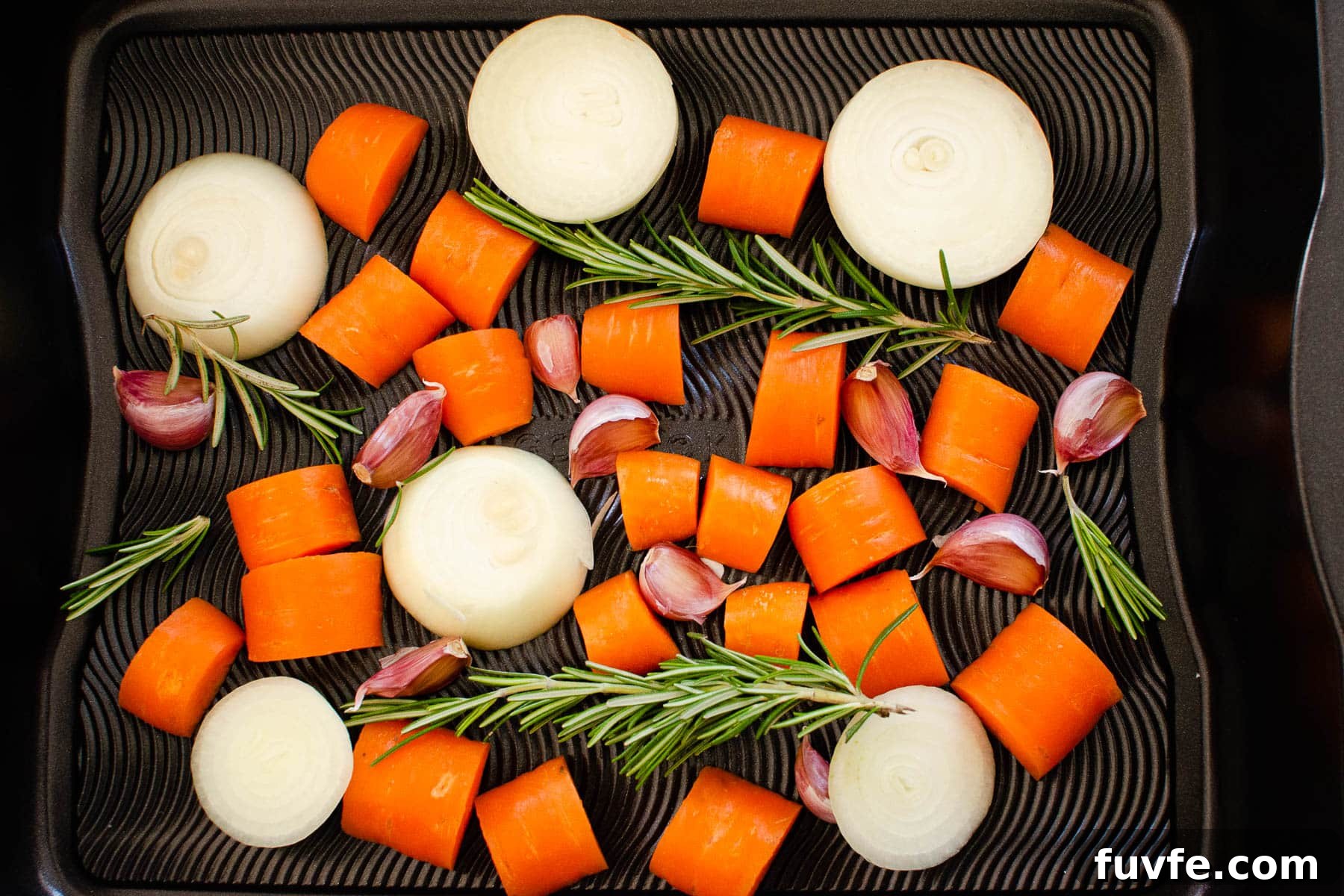 Chopped onion carrots garlic cloves and sprigs of thyme in a roasting tray
