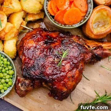 Slow Cooked Leg of Lamb on a wooden board with peas, roast potatoes, carrots and Yorkshire puddings