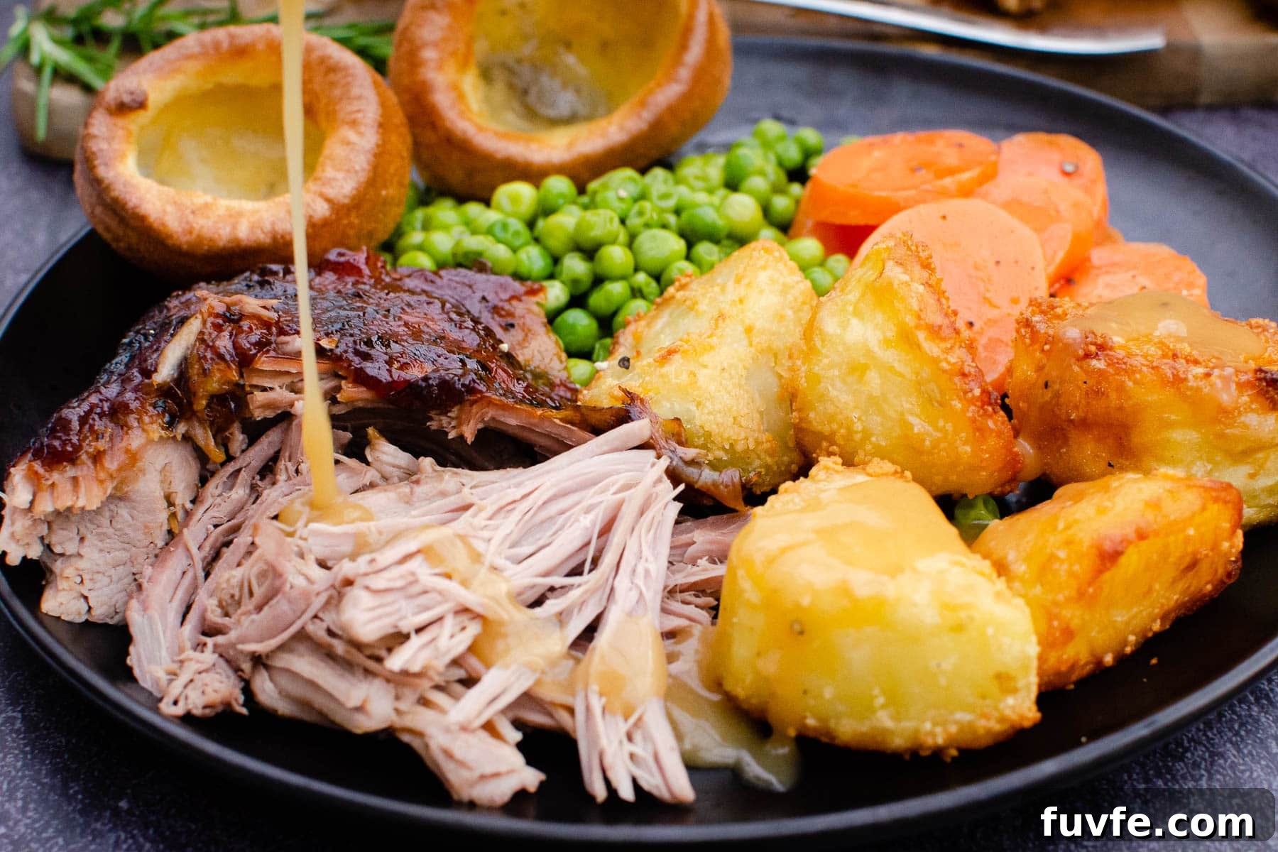 Slow roast leg of lamb served with roast potatoes, carrots,peas and Yorkshire puddings and lamb gravy being poured over the top