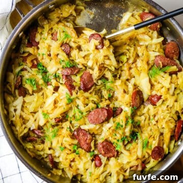 fried cabbage and sausage with dill and fresh parsley garnish in a skillet.