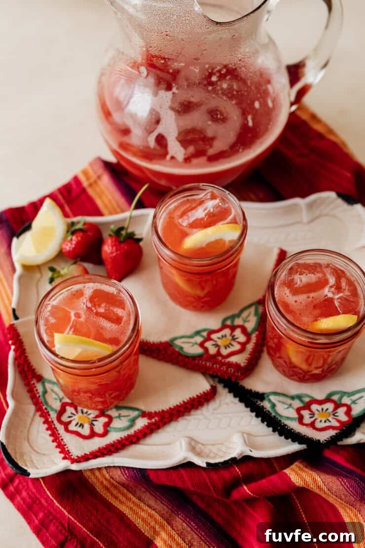 three mason jars of strawberry fruit tea with a pitcher of the sweet tea