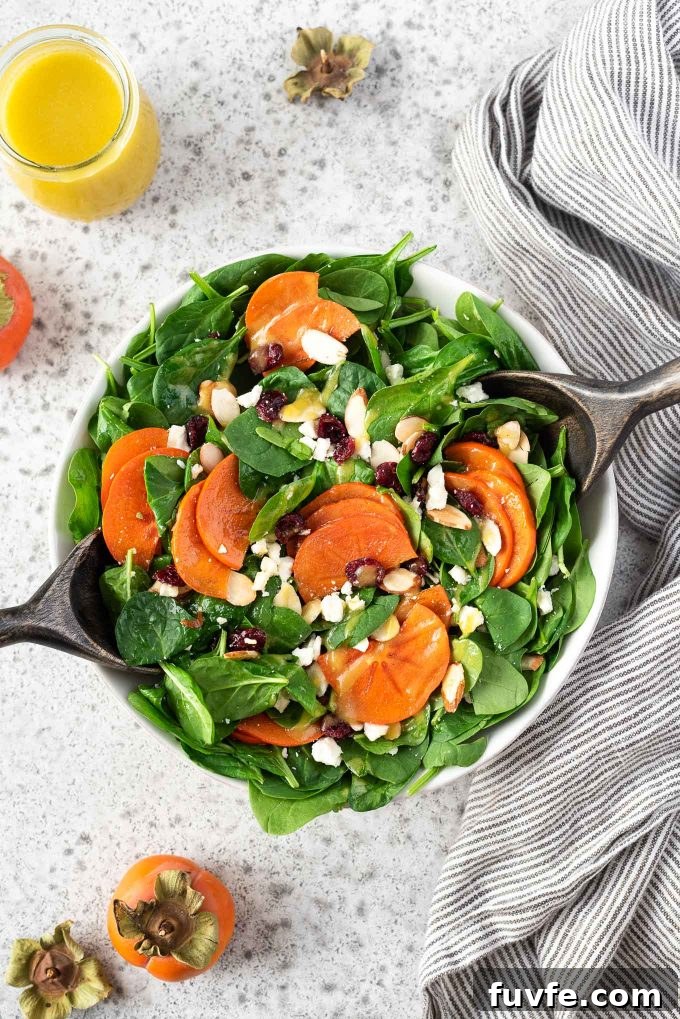 Persimmon salad in a bowl with salad servers