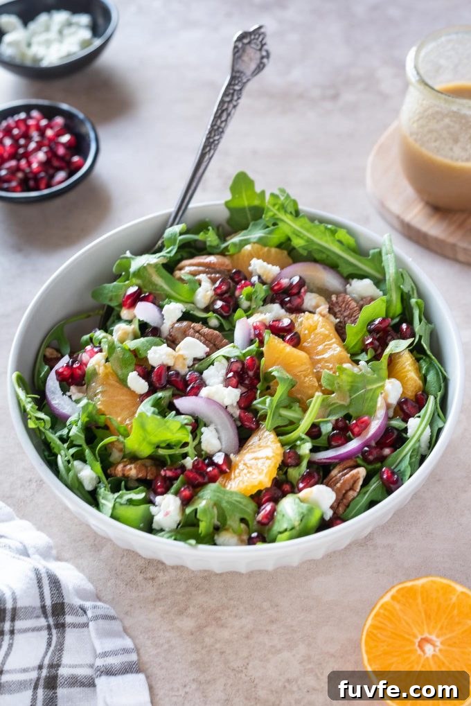 Arugula orange pomegranate salad in a white bowl with fork digging in