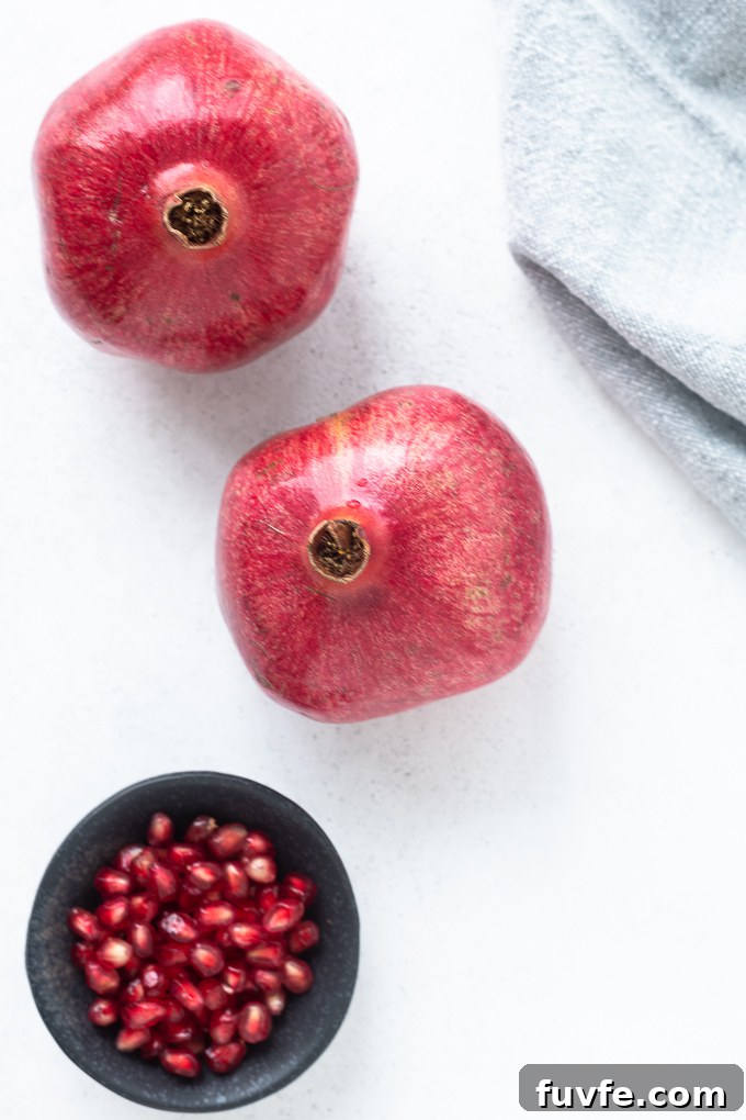 Two pomegranates next to bowl of arils
