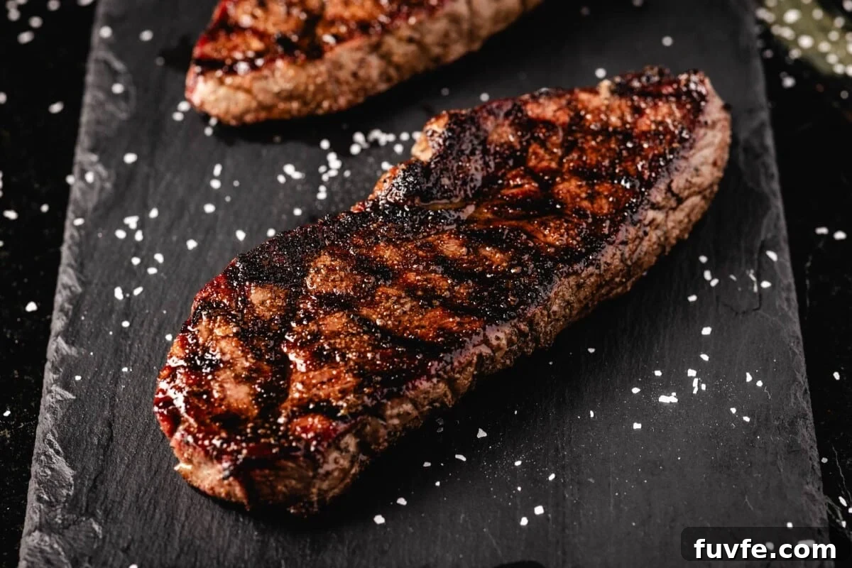 Grilled sirloins on black serving platter sprinkled with salt.