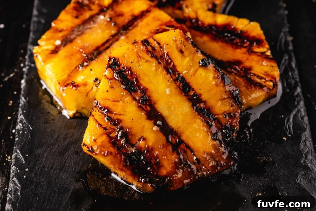 Grilled pineapple slices stacked on a black countertop.