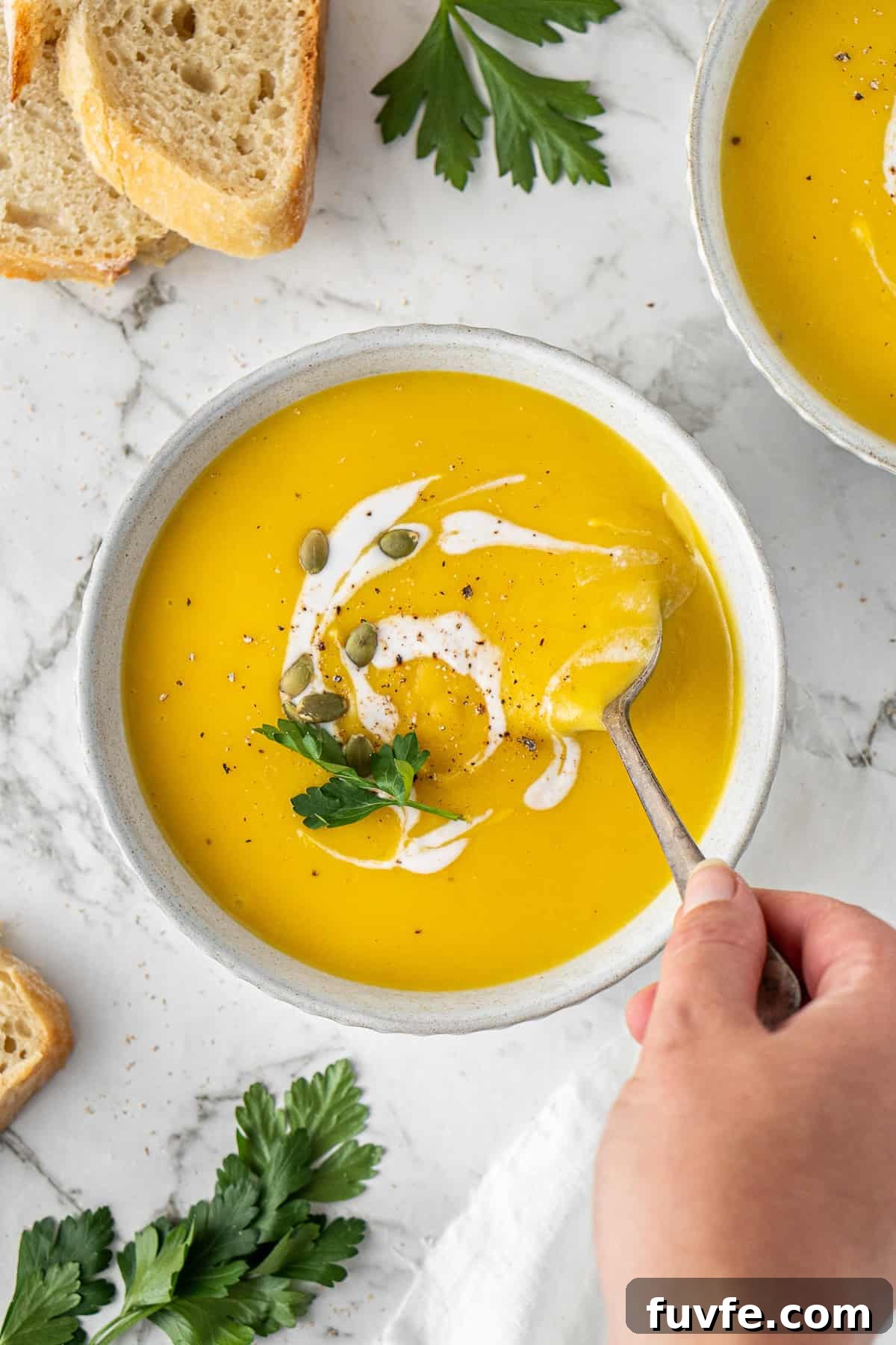 Grandma’s Creamy Pumpkin Soup Recipe 11 Dairy free pumpkin soup in a bowl with a hand putting in a spoon.