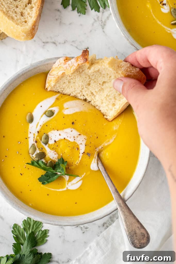 Grandma’s Creamy Pumpkin Soup Recipe 10 A hand dunking in a slice of fresh bread into the soup.