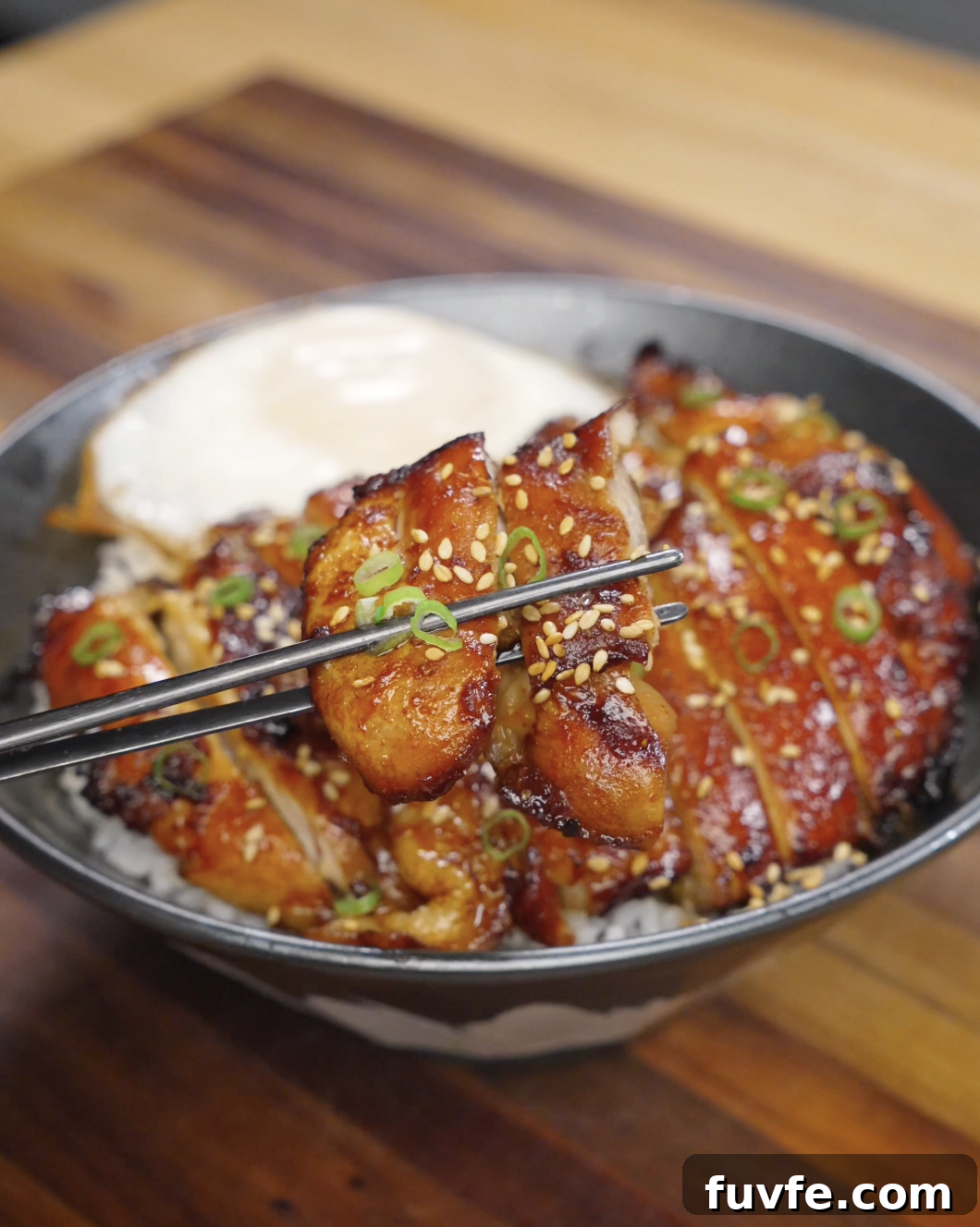 Chopsticks lifting a piece of caramelized chicken bulgogi coated in a glossy gochujang-based sauce, topped with sesame seeds and sliced scallions over a bowl of rice.