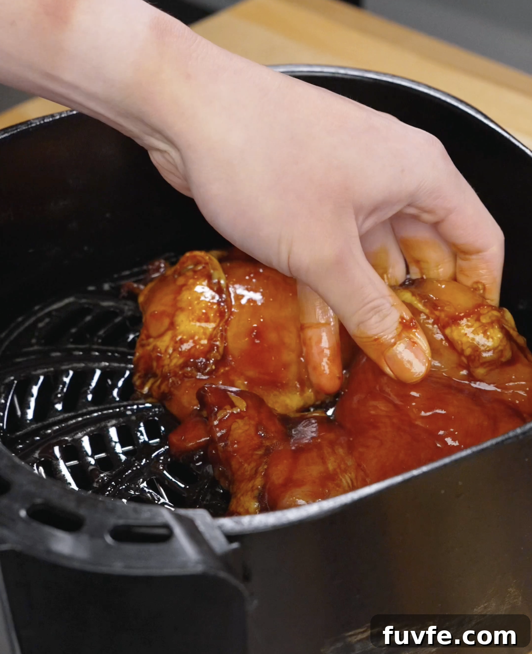 Marinated chicken thighs being placed into an air fryer basket, coated in a rich bulgogi sauce ready to cook until caramelized and juicy.