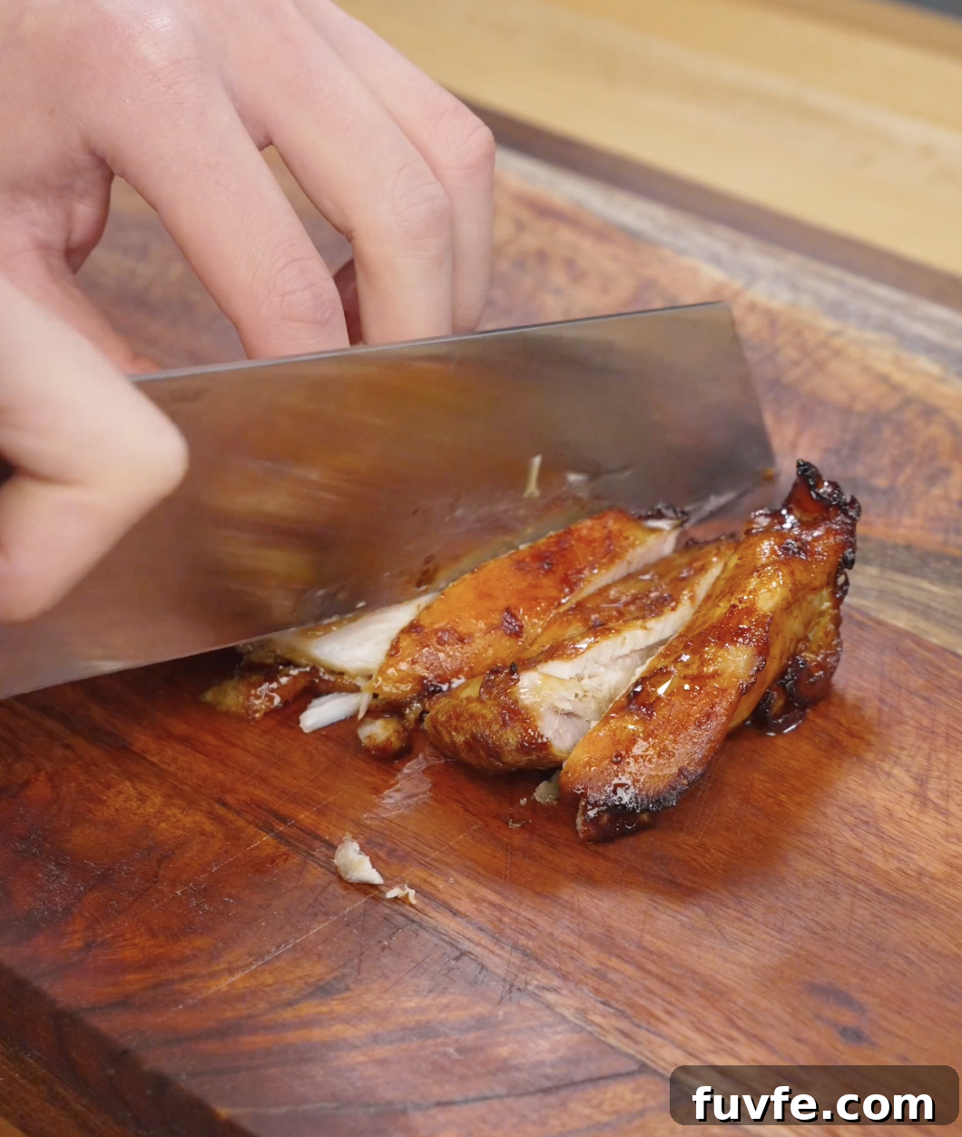 Cooked chicken bulgogi being sliced into thin strips on a wooden cutting board, revealing juicy interior and caramelized exterior from the marinade.