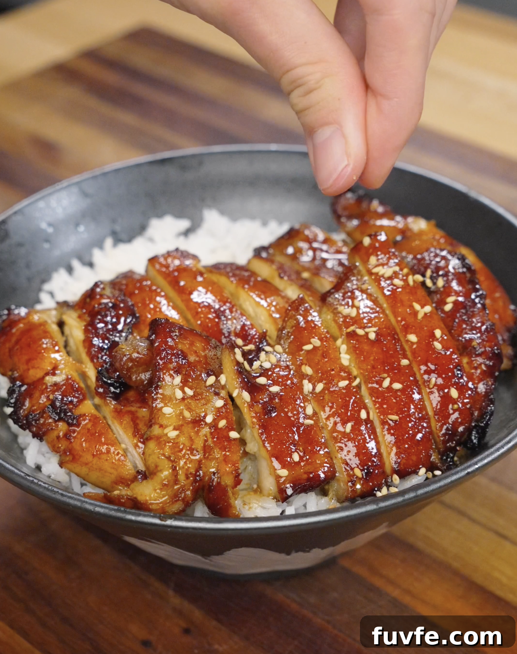 Sesame seeds being sprinkled over sliced chicken bulgogi on top of rice, adding texture and nutty flavor to the finished dish.