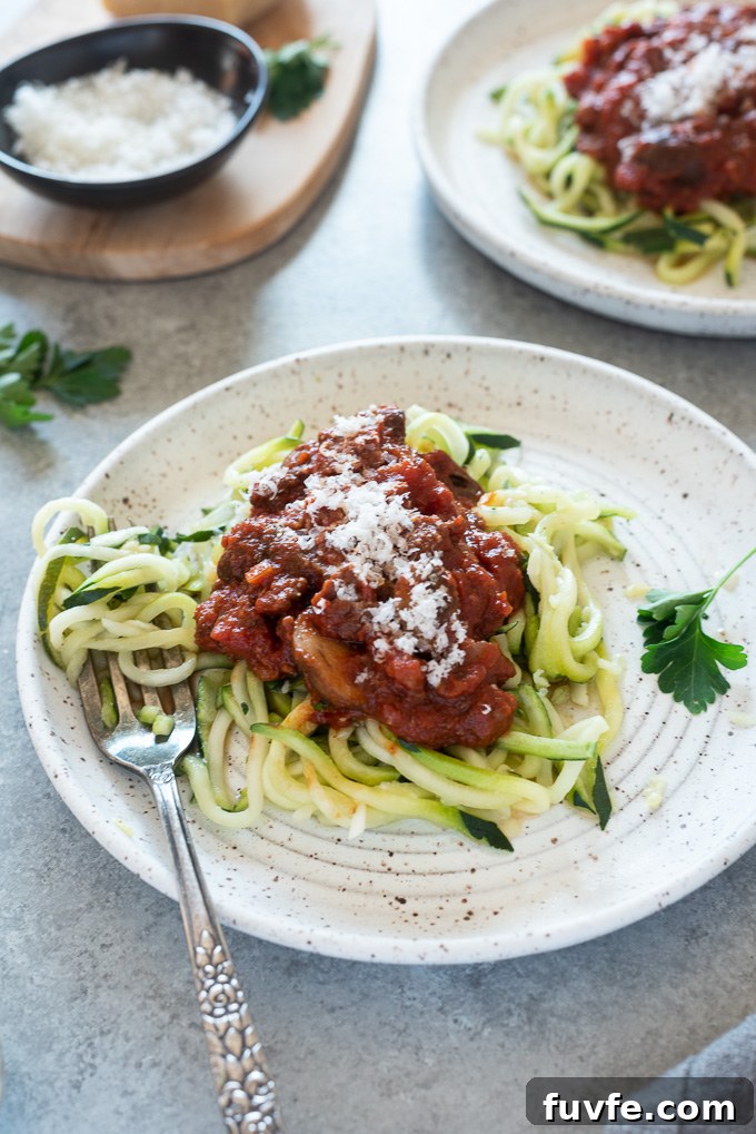 Plate of zucchini noodles topped with meat sauce and parmesan cheese