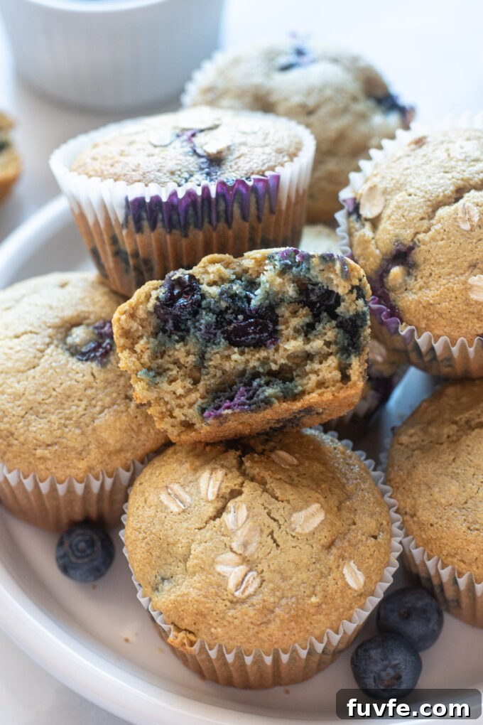 Blueberry oatmeal muffins on a plate with top muffin cut in half.
