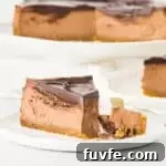 slice of amaretto cheesecake on a plate with the rest of the cheesecake on a cake stand in the background
