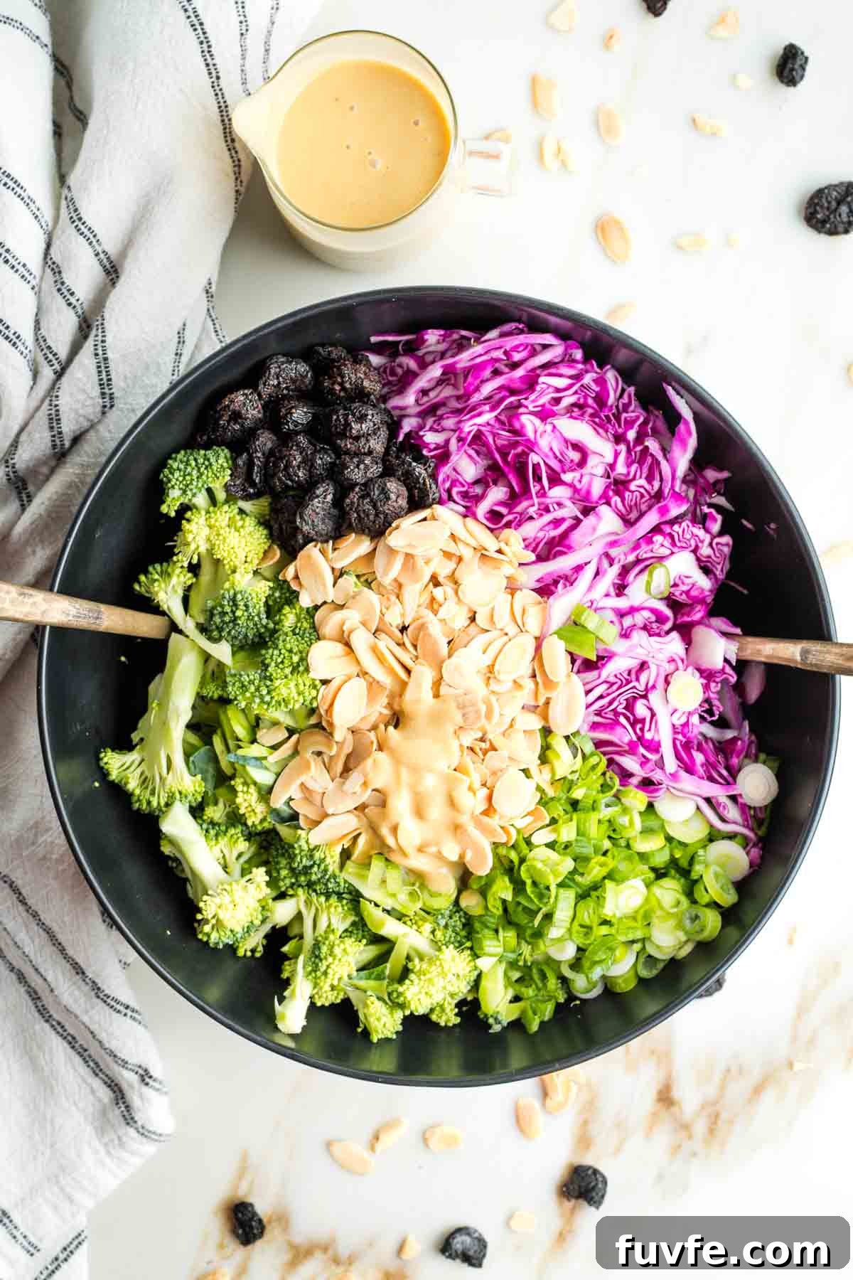 Dressing in the center of a prepped salad with broccoli, cabbage, nuts, dried fruit and scallions.