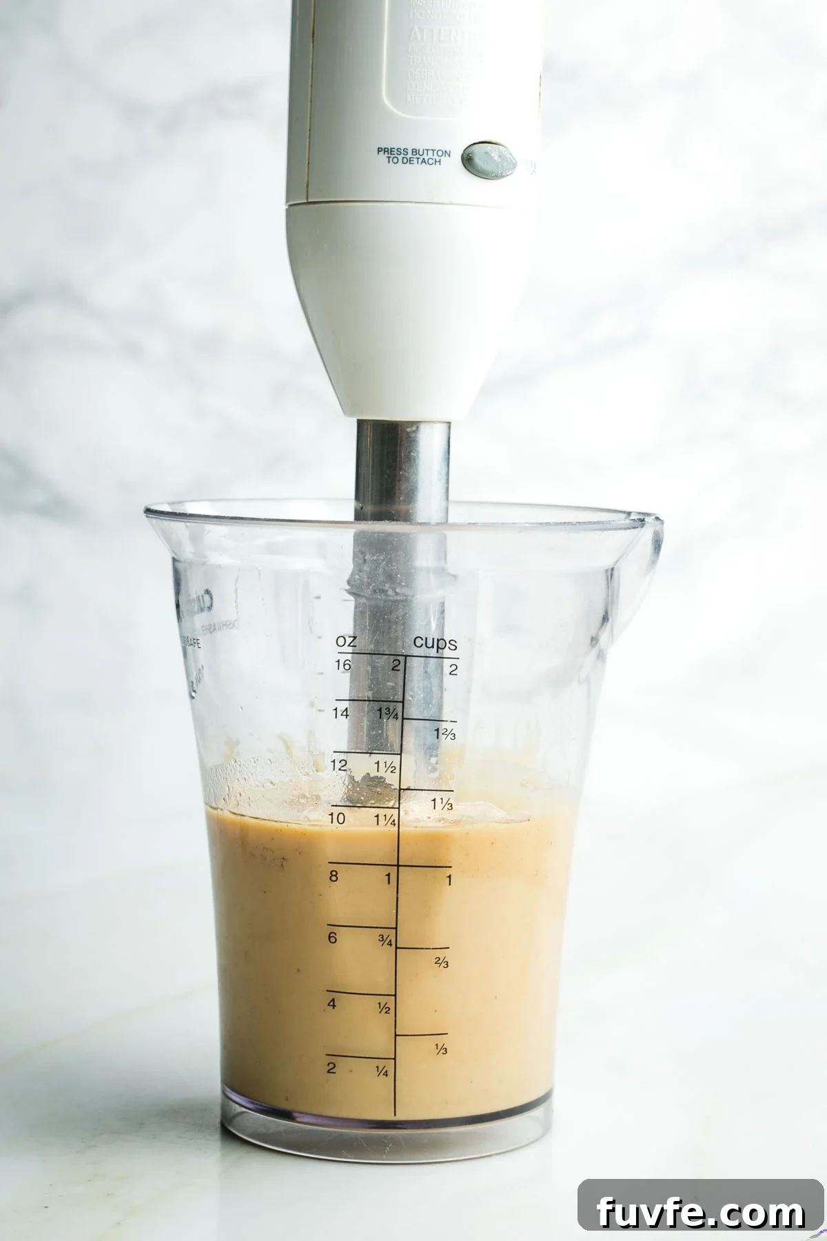 Immersion blender creating a creamy light tan dressing in a cup.